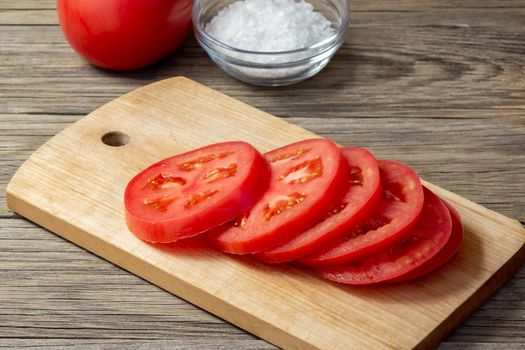Tomato sliced into round slices on a wooden cutting board.