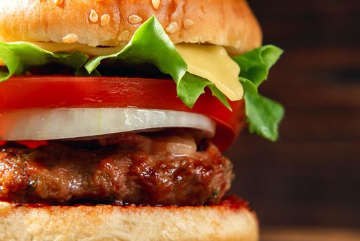Fresh homemade burger with meat cutlet, tomatoes, lettuce, cheese and onions on a wooden background, close up.