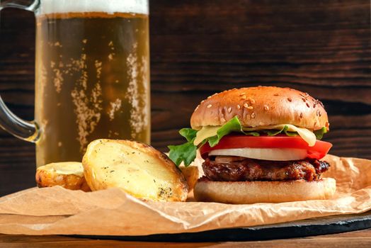 Homemade cheeseburger with beer mug on wooden background.