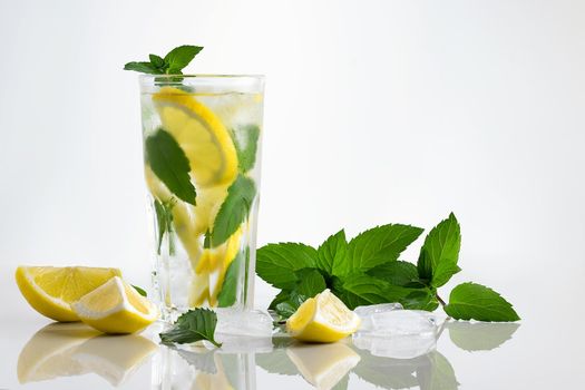 Fresh homemade cocktail in a tall glass with lemon, mint and ice on a white background, copy space.