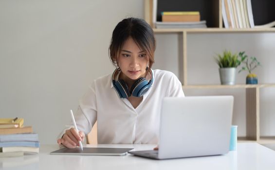 Portrait of female worker working from home with digital tablet, laptop and headphone in home office room