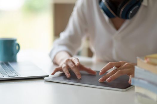 Close up of female worker working from home with digital tablet, laptop and headphone in home office room