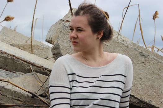 A portrait of an outdoor girl sits in a field on large concrete slabs. High quality photo