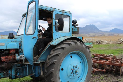 A large old blue tractor with plows field in the fall. High quality photo