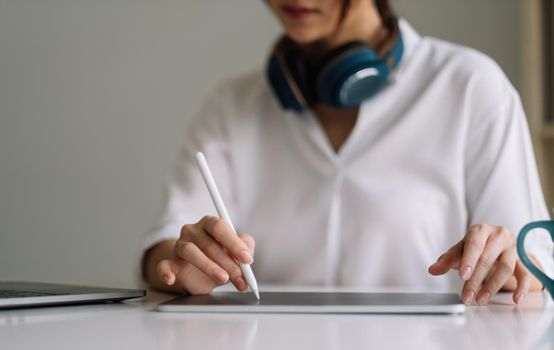 Close up of female worker working from home with digital tablet, laptop and headphone in home office room