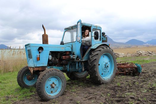 The girl on the tractor in the field. Plow the tractor land in the fall. Agricultural work. High quality photo