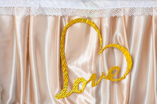 A golden heart with the inscription love on a fabric background.