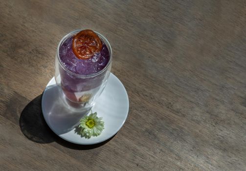 Glass of soda drink with lemonade, orange mixer butterfly pea juice (Anchan) cold refreshing drink or beverage with ice on wooden table. Copy space, Selective focus.