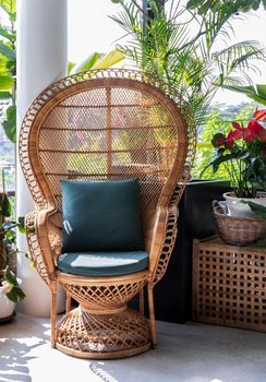 Peacock wicker rattan chair and flowers in living room overlooking the garden. Wicker chair interior decor.