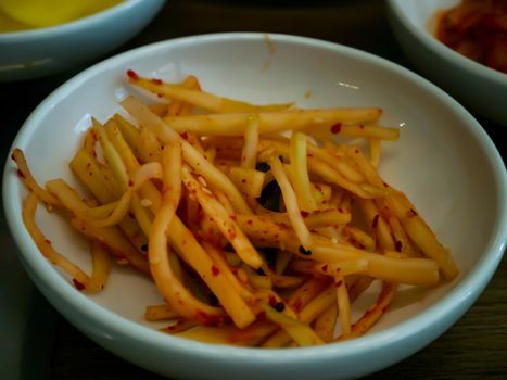 Orange pickled radish in a white cup for eating. Asian side dish Pickled radish, Korean food traditional. No focus, specifically.