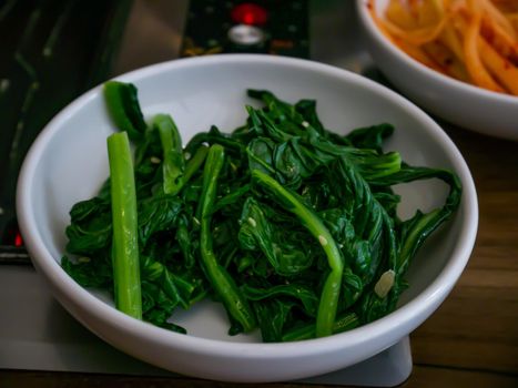 Mixed soy sauce and spinach with sesame Namul in a white cup for eating. Korean food traditional. No focus, specifically.