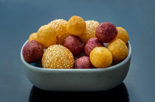 Fried Sweet Potato Balls with sesame with Deep fried purple and yellow sweet potato balls (Quail candy eggs) on marble table. Thai Traditional dessert snack made from cassava flour (tapioca starch) and sweet potato, Selective focus.