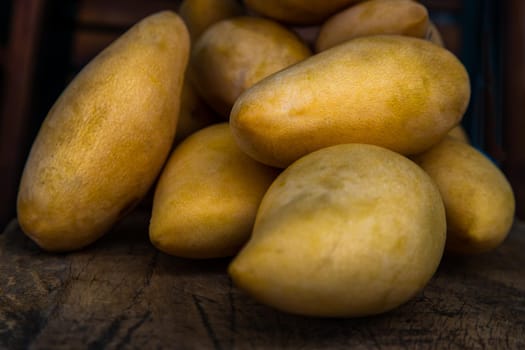 Ripe yellow barracuda mango fruit (Nam Dok Mai) on the old wooden table background. Tropical healthy fruit background, Selective focus.