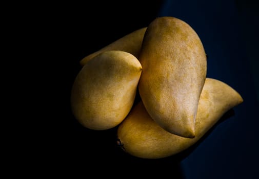 Ripe yellow barracuda mango fruit (Nam Dok Mai) on black table background. Tropical healthy fruit background, Selective focus.