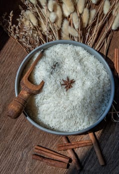 Thai jasmine rice in bowl with wooden spoons, Star anise and Dried flowers on old rustic wooden background. Healthy food and diet concept. Top view. Flat lay. Selective focus.