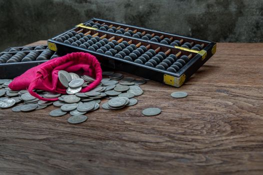 Vintage wooden hand abacus with pile of money coins from red cloth bag on rustic old wooden table. Concept for making business and saving money of chinese, Copy space, Selective focus.