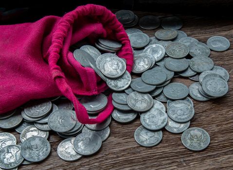 Pile of money coins from red cloth bag on rustic old wooden table. Concept for growth business and saving money. Copy space, Selective focus.