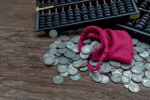 Vintage wooden hand abacus with pile of money coins from red cloth bag on rustic old wooden table. Concept for making business and saving money of chinese, Copy space, Selective focus.
