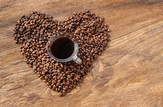 Coffee mug over on heart shape made from Pile of coffee beans on wooden texture with background for Valentines Day. Symbol of Love to coffee, Selective focus.