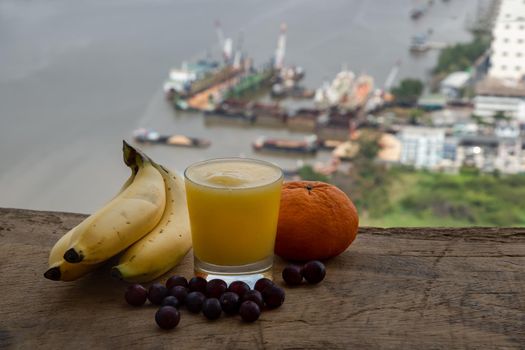 Healthy ripe Yellow Mango Smoothie in Glass and Banana, Orange and Grape rustic old wooden table with river view. Tropical fruit concept. Selective focus.