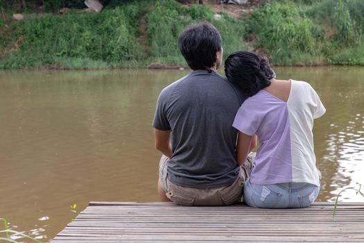 Rear view of young couple sitting in the border of a canal and watching river movement with together. Selective focus.