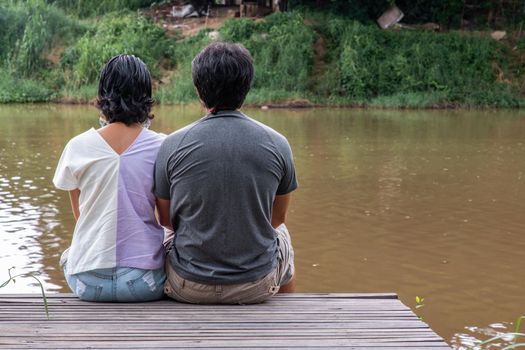 Rear view of young couple sitting in the border of a canal and watching river movement with together. Selective focus.