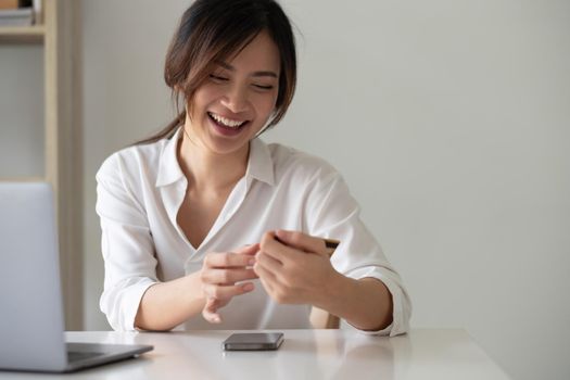 Happy asian woman using her credit card for online shopping at home office