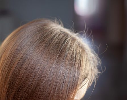 A woman's head with a parting of gray hair that has grown roots due to quarantine. Brown hair on a woman's head close-up.