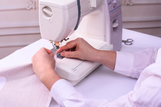 production of bed linen on a sewing machine. women's hands sew light cotton fabric.