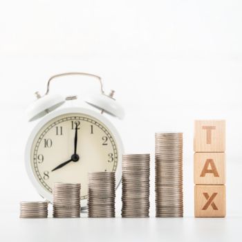 Concept of tax season approaching with wooden blocks, coins and alarm clock over white background.