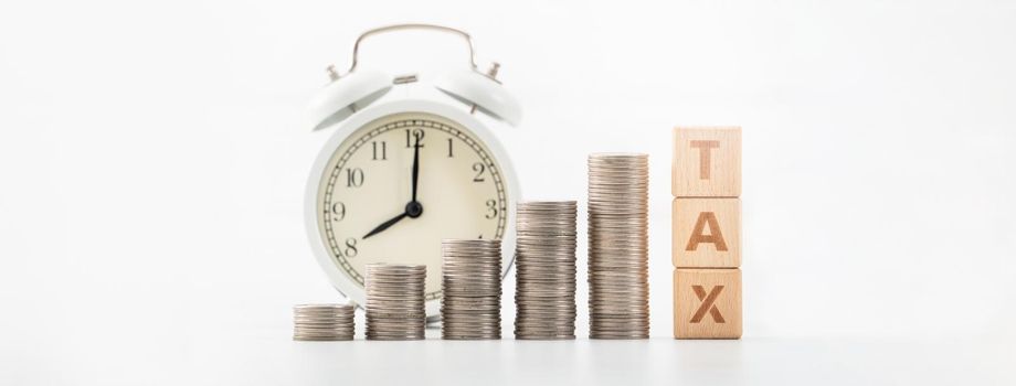 Concept of tax season approaching with wooden blocks, coins and alarm clock over white background.