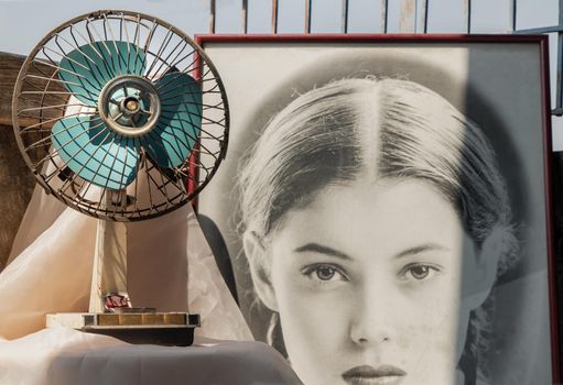Bangkok, Thailand - 06 Feb 2021 : Old vintage blue electric fan and Old french movie poster frame on Old mortar wall in house in retro style. Selective focus.