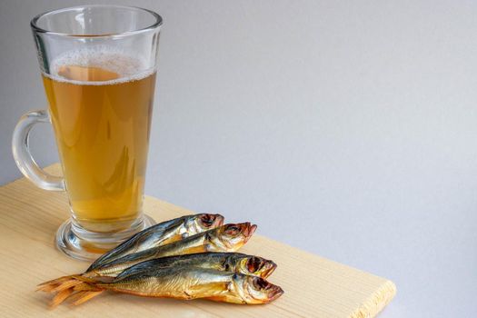 Smoked horse mackerel and beer in a glass on a wooden board on a gray background. Oktoberfest Holiday Concept.