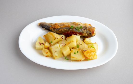 Fried fish and potatoes on a white plate on the table.