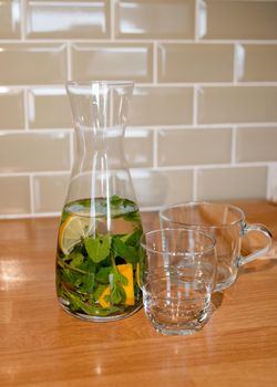 fresh water with lemon and mint in decanter and glass on table in kitchen