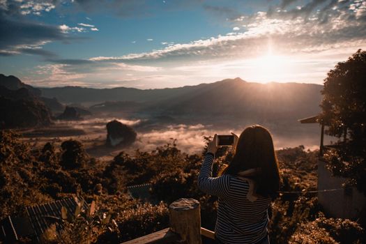 The girl take photo with smart phone on balcony bar at Phu Lang Ka mountain landmark in Phayao province Thailand