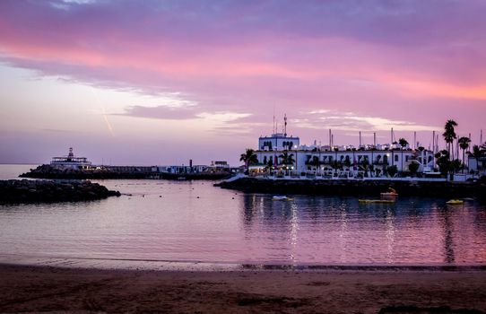 Wide shot of a beach with white buildings and a purple sky at dusk