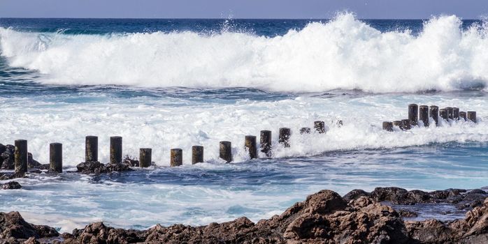 WIde shot of foamy waves clashing against a rocky beach on a sunny day