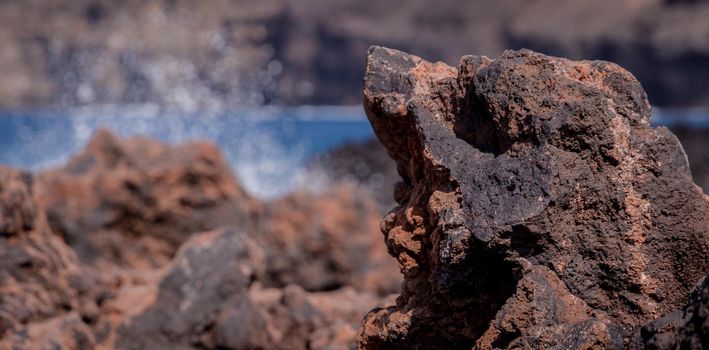Detail of a dark volcanic rock on a sunny day with the sea in the background