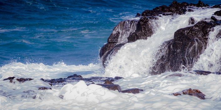 Detail of the sea foam after a wave covering some dark volcanic rock in the sun