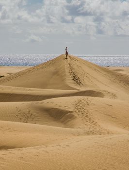 Two people climbing a sand dune in the beach on a sunny day with the sea at the background