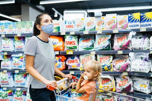 Shopping with children during the coronavirus epidemic. Mother and baby in protective mask buying fruit in the supermarket. Mom and little girl household chemicals in the store. High quality photo