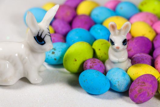 Easter bunnies with colorful speckled candy eggs on textured white surface