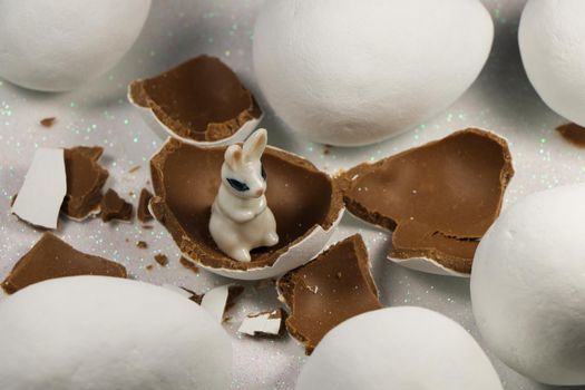 White bunny rabbit in broken chocolate candy Easter eggshells with large chocolate candy eggs