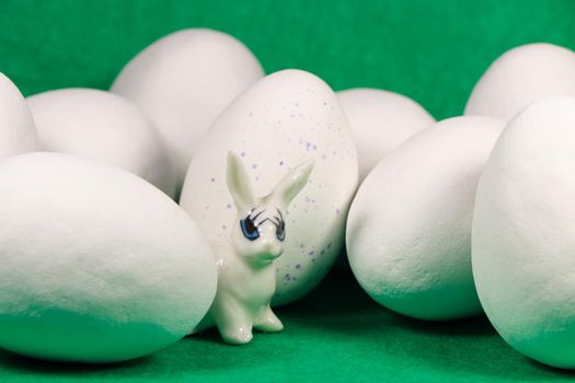 White rabbit with large chocolate candy Easter eggs and one blue speckled egg on green