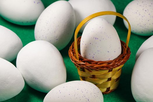 Large white and blue speckled chocolate candy Easter eggs with woven basket on green