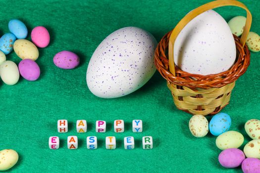 Happy Easter text beads with speckled chocolate candy eggs and weave basket on green