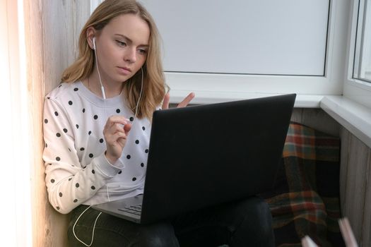 Young woman sitting on balcony next to laptop. Online education. Stay home concept. Work from home. Earphones