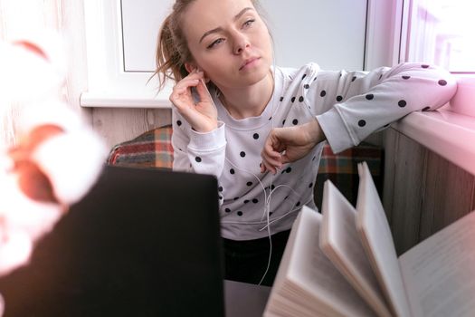 Young woman sitting on balcony next to laptop. Online education. Stay home concept. Work from home. Earphones