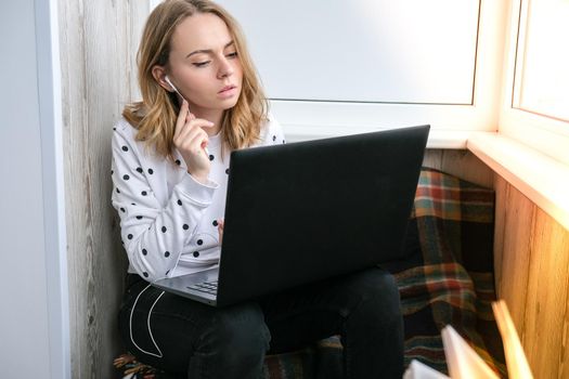 Young woman sitting on balcony next to laptop. Online education. Stay home concept. Work from home. Earphones